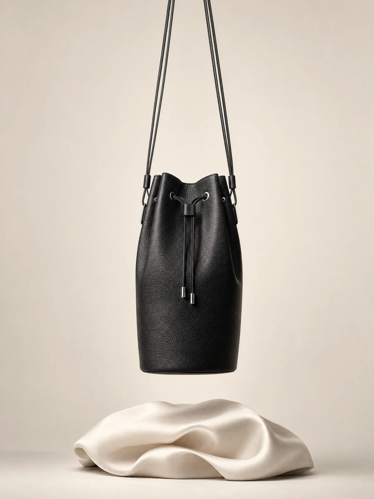 Bolso saco negro suspendido sobre una forma de satén marfil