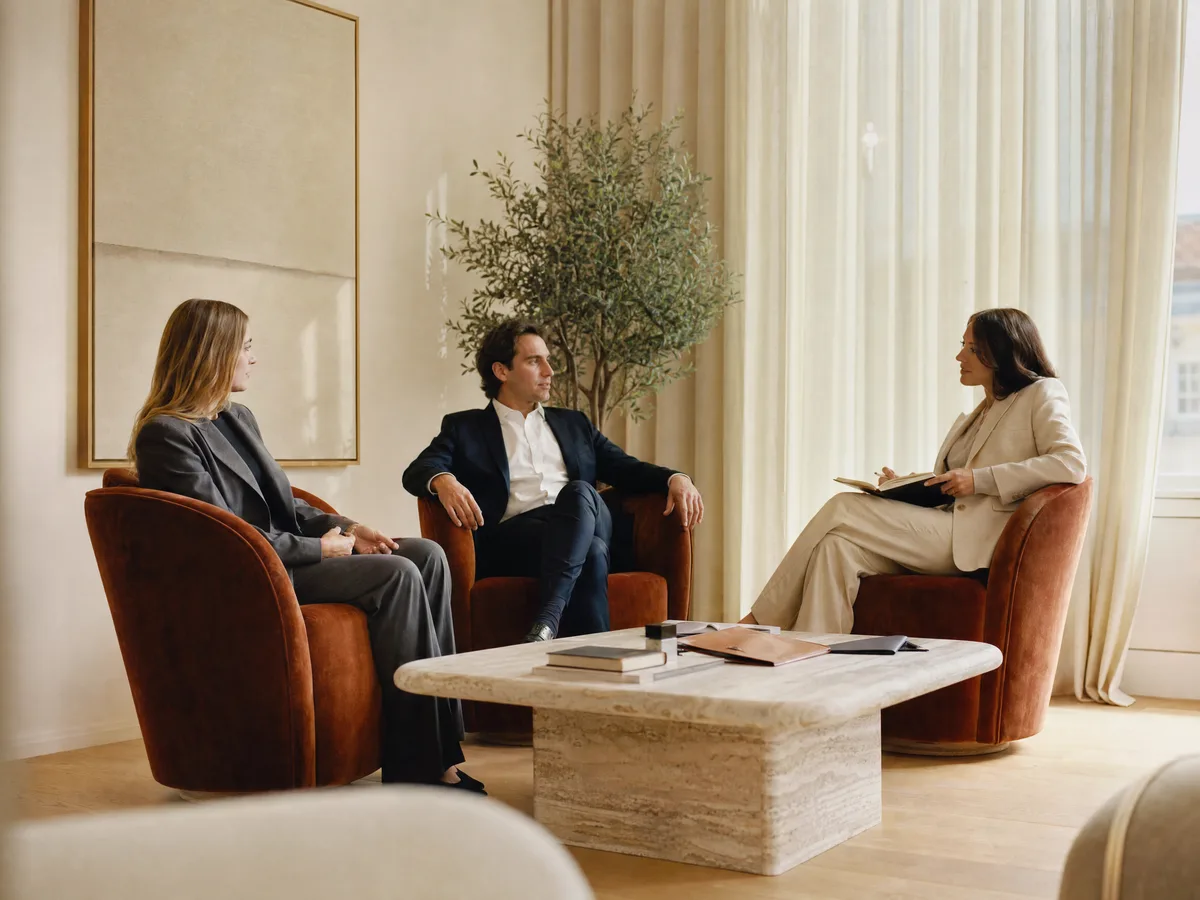 Tres personas conversando en la sala de reuniones del despacho, en butacas terracota