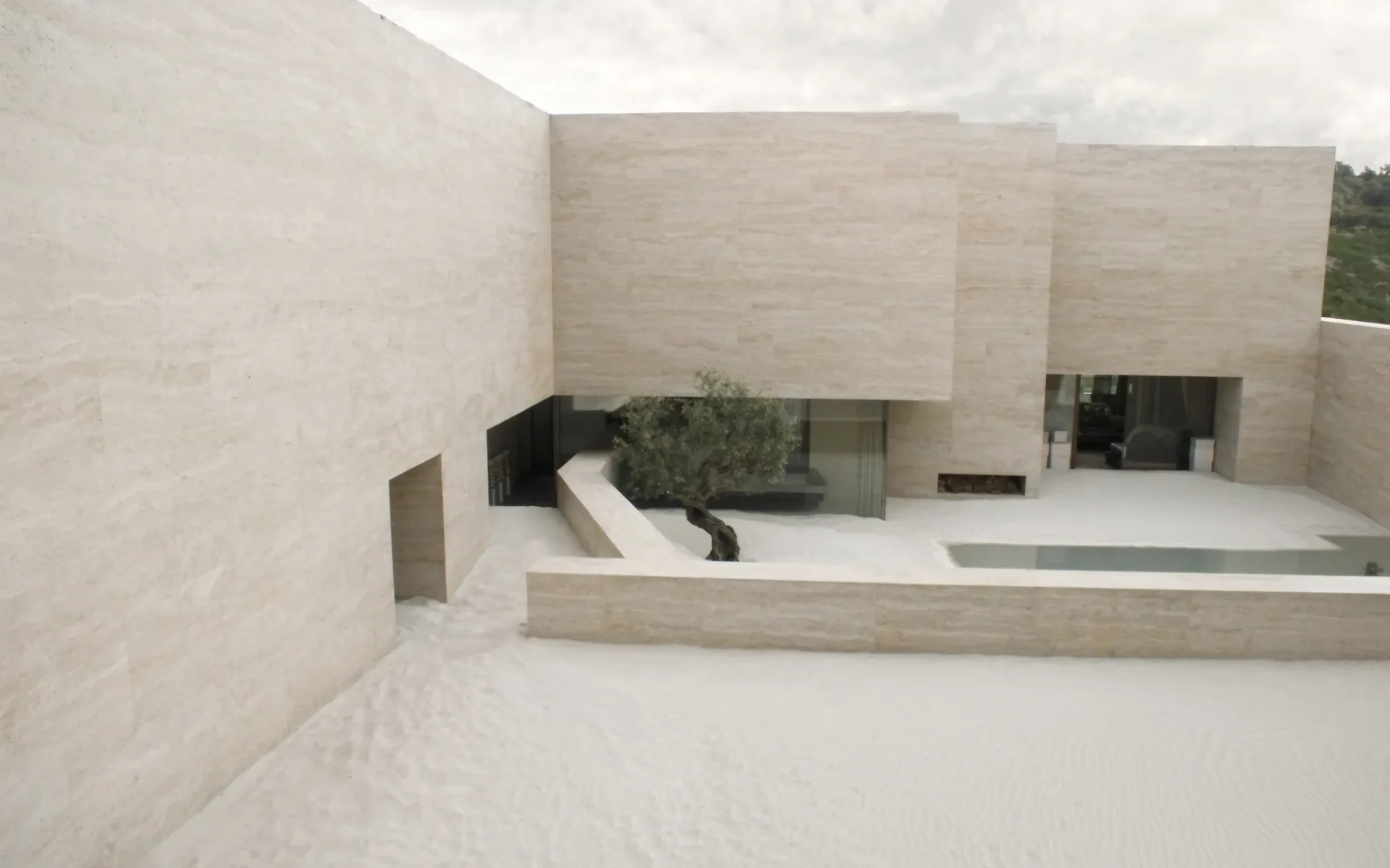 Casa de piedra clara organizada alrededor de un patio con un olivo