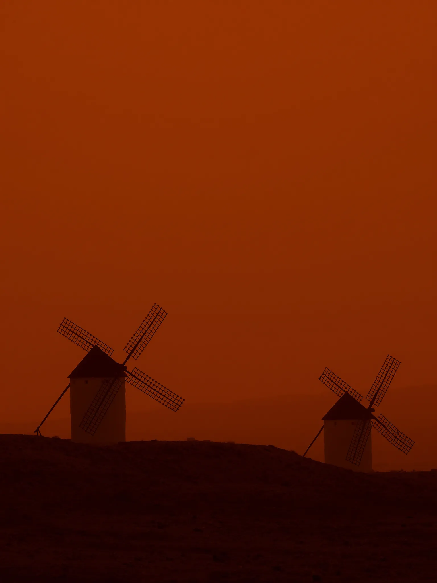 Molinos de Consuegra en silueta contra un cielo naranja