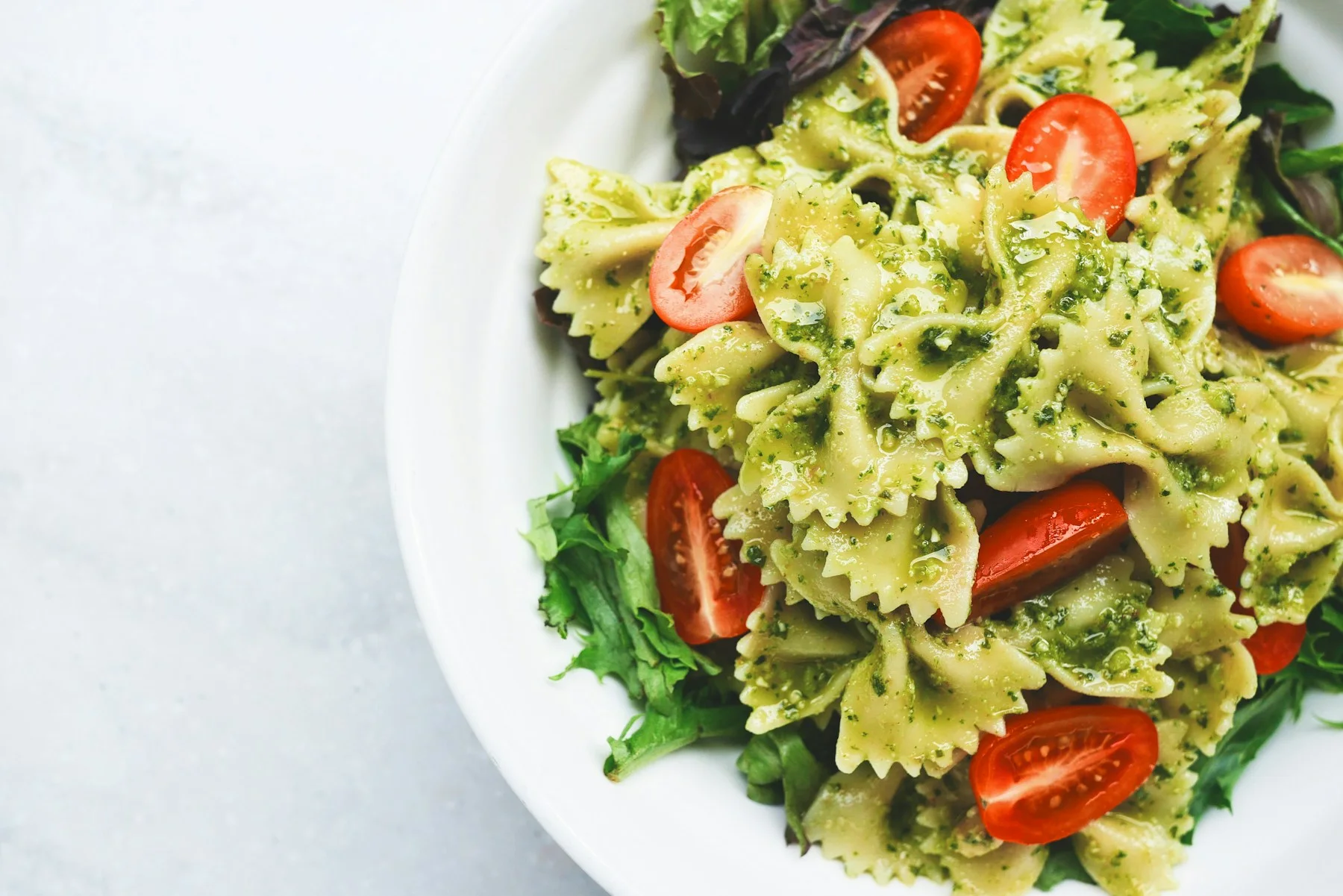 Pasta al pesto con tomates y albahaca sobre un plato blanco