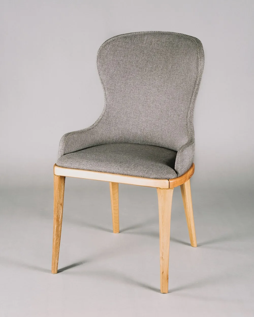 Una silla de tejido gris y madera clara junto a una pared serena