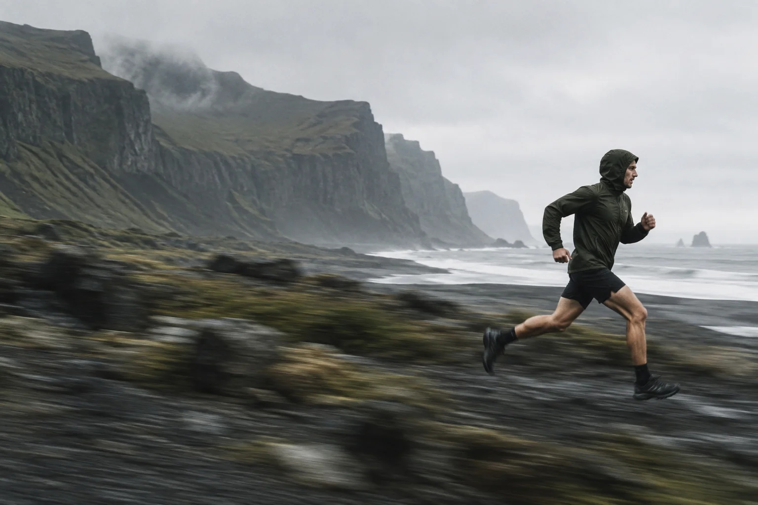 Atleta con chaqueta oliva corriendo por una costa volcánica